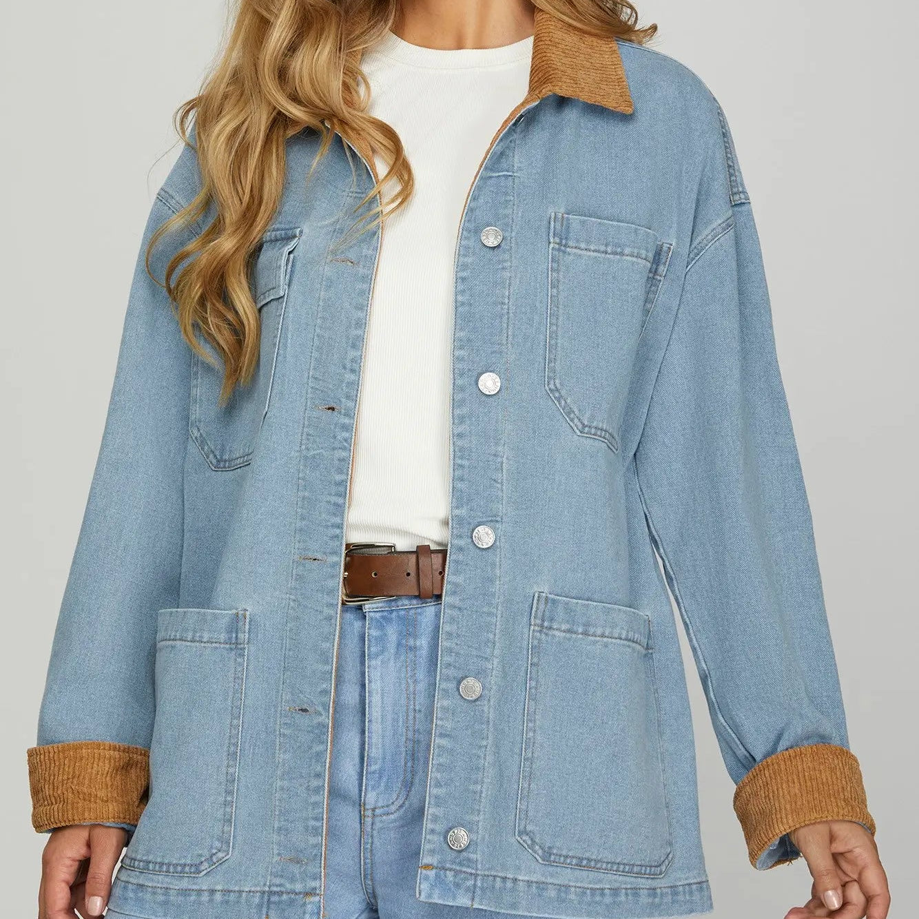 Woman wearing a light blue denim jacket with brown cuffs and collar on a gray background