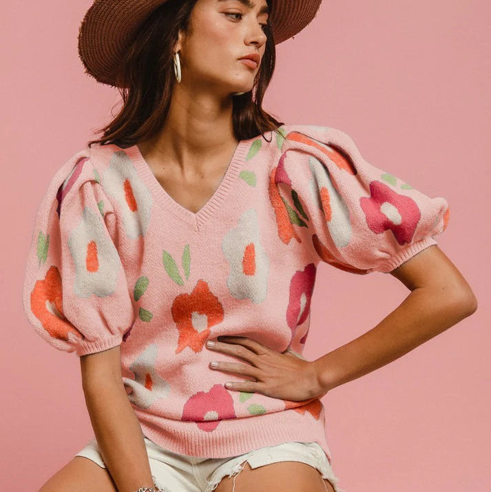Woman wearing a pink floral sweater and straw hat on a pink background