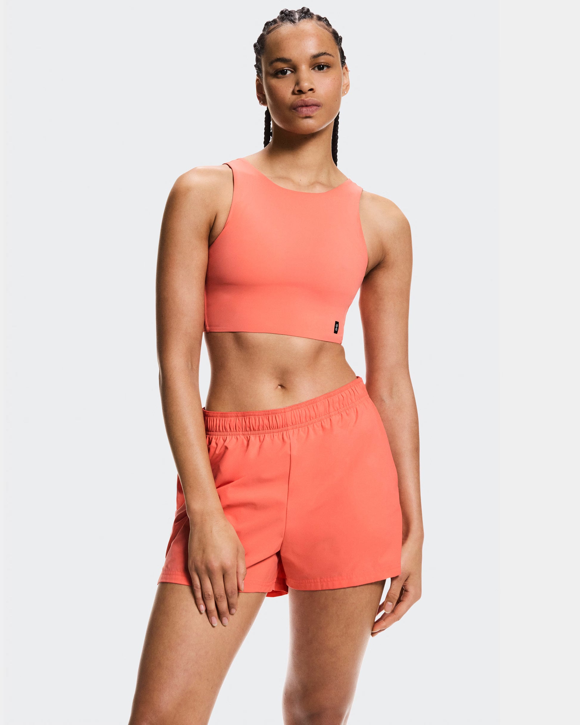 Woman wearing a coral sports bra and shorts set on a white background