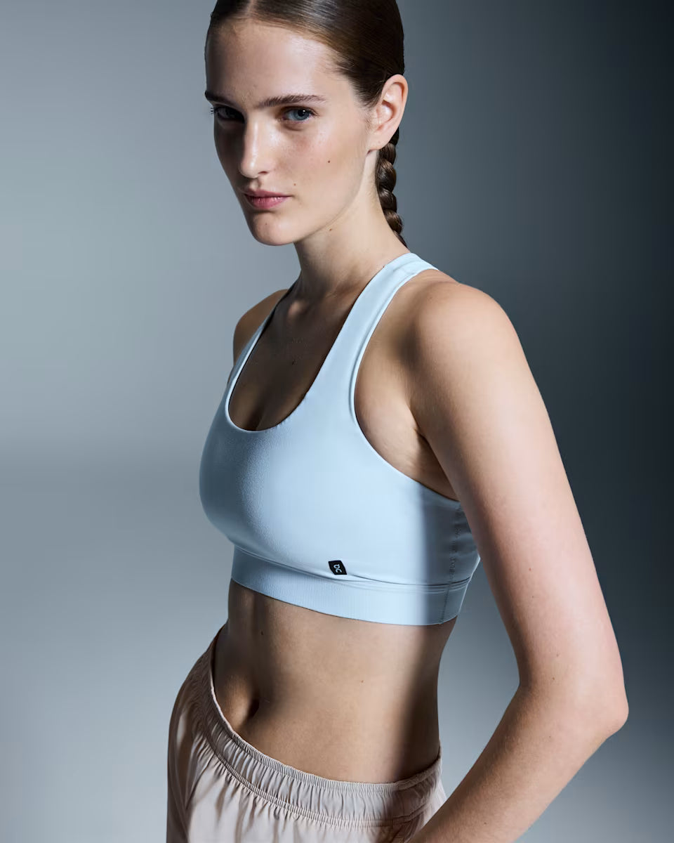 Woman wearing a light blue sports bra and beige shorts on a gray background
