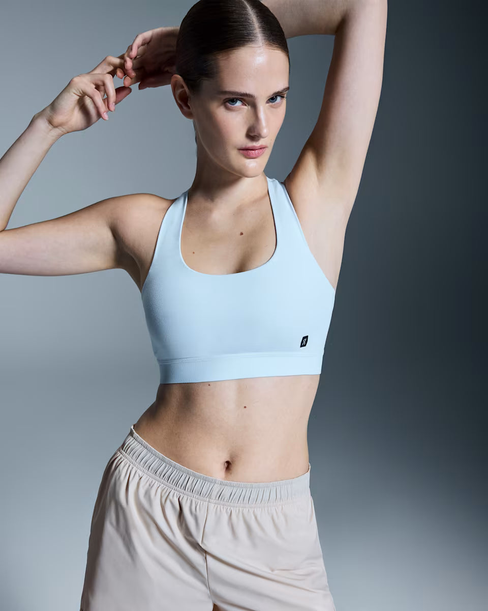 Woman wearing a light blue sports bra and beige shorts on a gray background