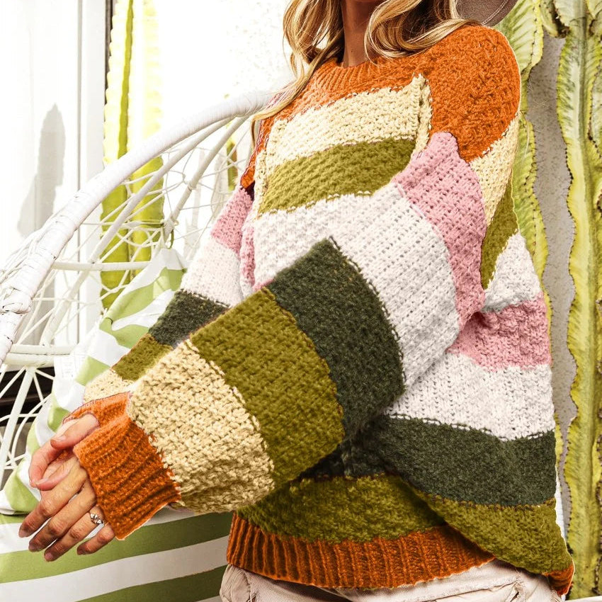 Woman wearing a colorful striped sweater and hat in front of a cactus plant.