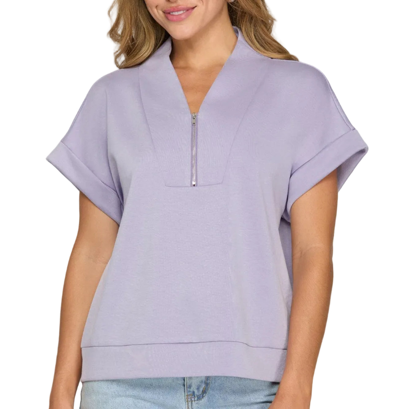 Woman wearing a light purple zip-up top and blue jeans on a plain background