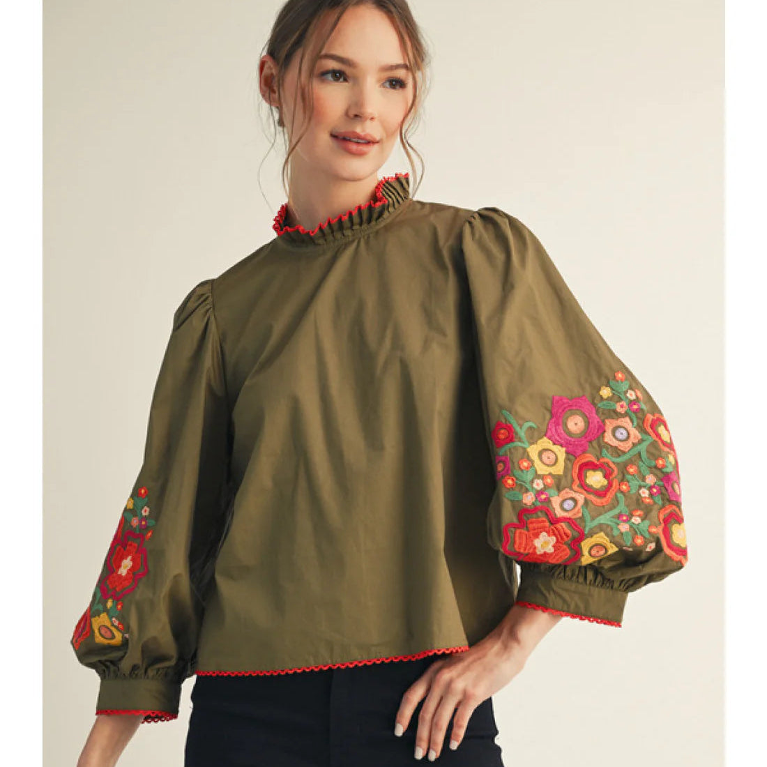 Woman wearing a green blouse with colorful floral embroidery on a beige background