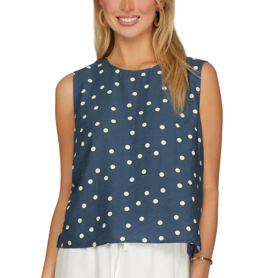 Woman wearing a navy sleeveless top with white polka dots on a plain background