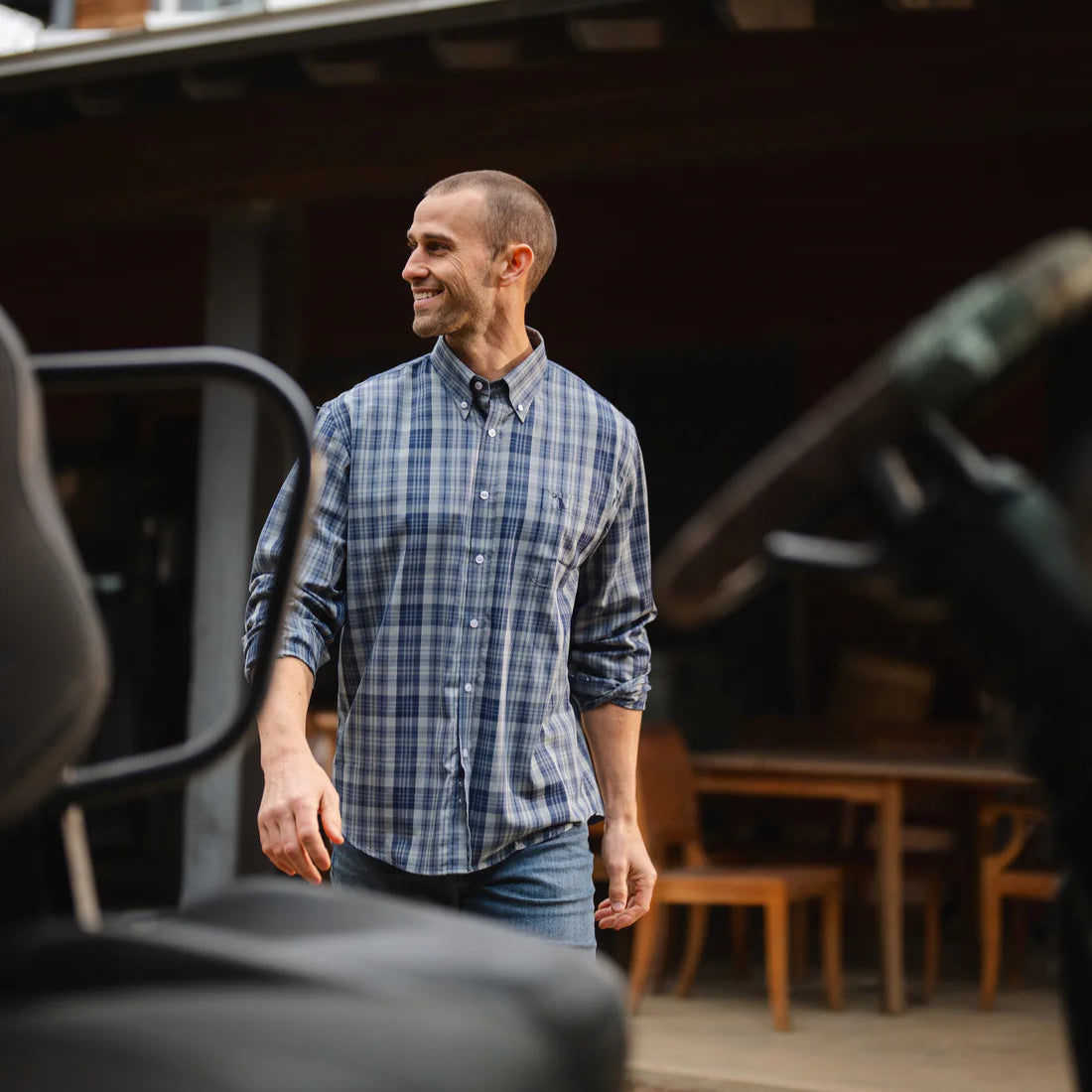 Man standing outside a wooden cabin wearing a plaid shirt.