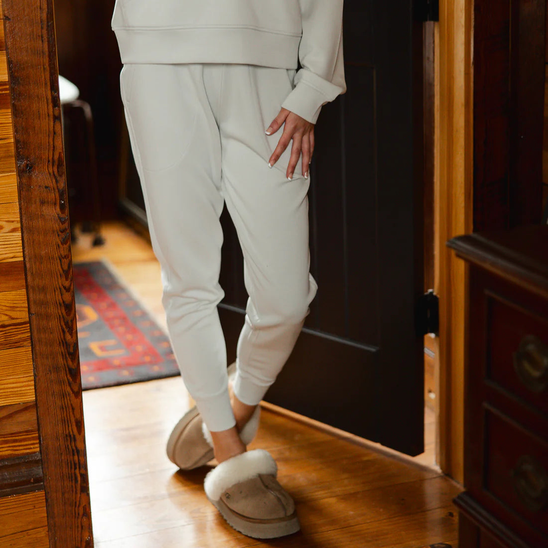 Person wearing a light gray hoodie and pants standing in a doorway.