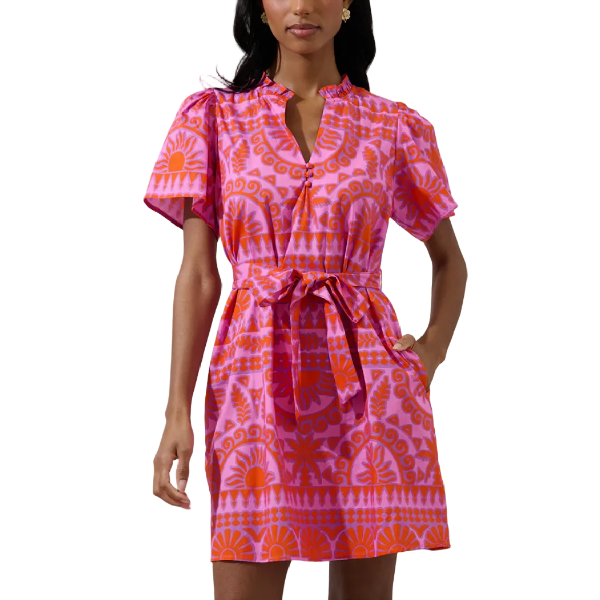 A woman modeling a short-sleeve pink dress with an orange and pink sunburst pattern, featuring a tie waist and V-neckline, set against a plain light gray background.