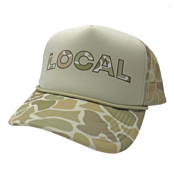 A trucker-style cap with a light sage green front panel and a desert camouflage pattern on the brim and mesh back. The word 'LOCAL' is embroidered across the front in a matching camouflage fill.