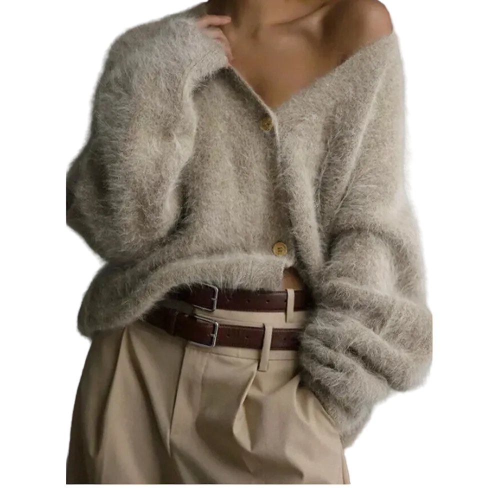 A person wearing a fuzzy off-the-shoulder cardigan in a light taupe-beige color, paired with beige trousers and a dark brown belt, against a plain gray studio background.