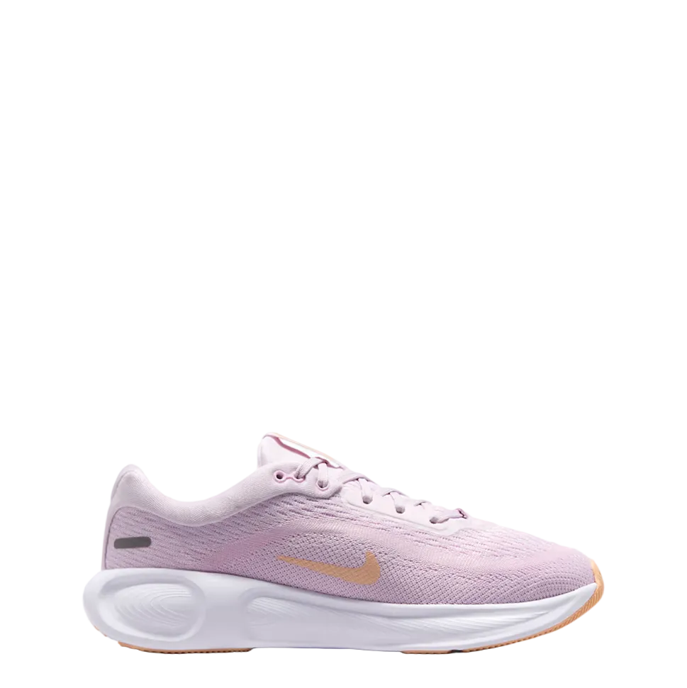 A Nike running shoe in light pink with a metallic gold Swoosh logo, a white midsole, and a gum outsole, shown from a side profile on a white studio background.