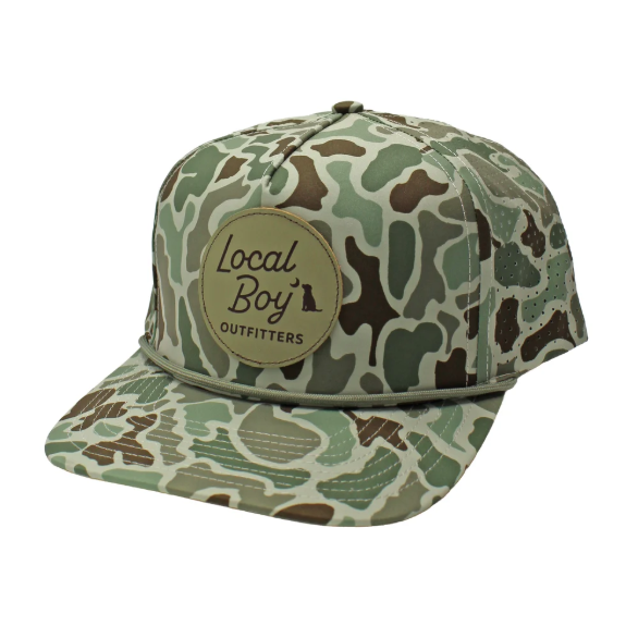 A camouflage baseball cap with a beige leather patch on the front that reads 'LOCAL BOY OUTFITTERS'. The cap features a green and brown woodland camo pattern with a light green rope detail across the brim, set against a plain white background.