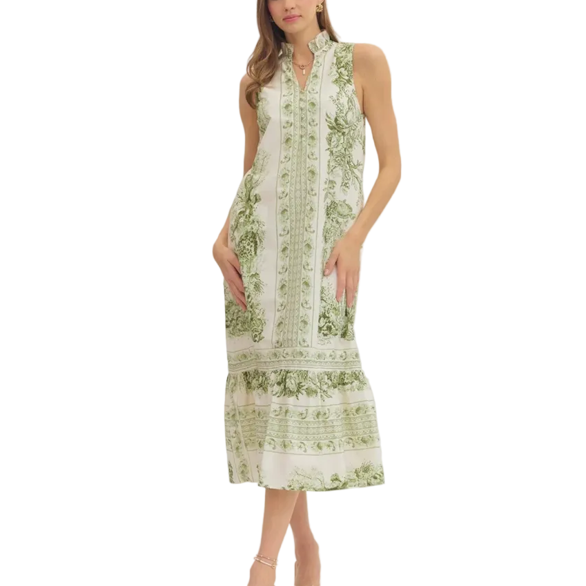 A woman modeling a sleeveless midi dress with a green botanical print on a white base, featuring a high collar and tiered skirt, set against a plain light gray studio background.