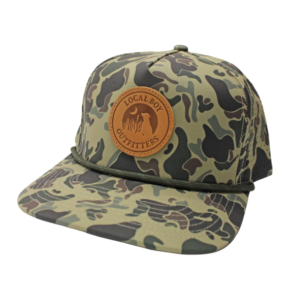 A camouflage baseball cap with a tan leather patch on the front that reads 'LOCAL BOY OUTFITTERS' and shows a deer graphic. The cap features a green and brown woodland camo pattern with a dark green rope detail across the brim, set against a plain white background.