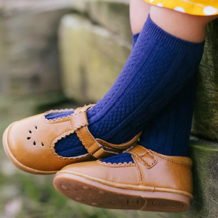 Child's feet wearing brown shoes and blue socks against a natural background